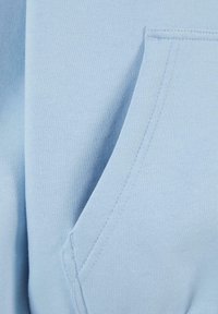 Hellblauer Sweatshirtstoff mit glatter Textur, ausgestattet mit einer Tasche mit sichtbaren Nähdetails und einem umgeschlagenen Saum.