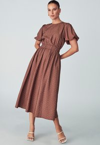 Robe midi marron dotée d'une taille élastique froncée, de manches courtes à volants et de pois blancs sur un tissu texturé.