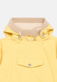 Κίτρινο αδιάβροχο μπουφάν με μπεζ ριμπ λαιμόκοψη, κλείσιμο με κουμπιά κράτησης και μπροστινή τσέπη με ασημί λεπτομέρεια κουμπιού. Λείο υλικό.