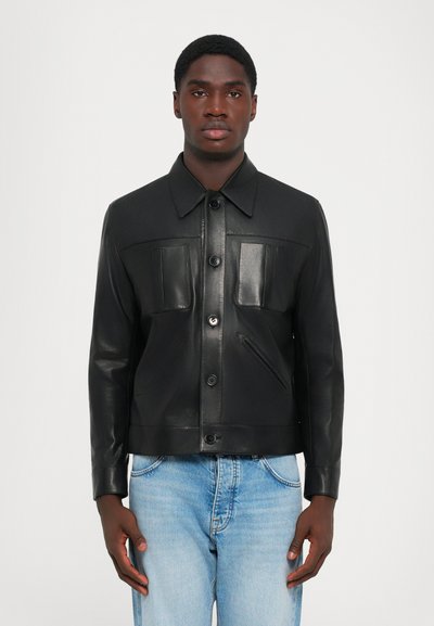 Sort læderjakke med krave, knaplukning, to brystlommer og en sidelomme. Glat tekstur med skræddersyet design.