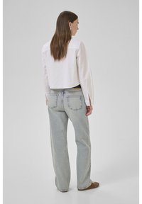 Camicia bianca tagliata con maniche lunghe, abbinata a jeans chiari e larghi. Accenti in hardware argentato sulle tasche posteriori dei jeans.