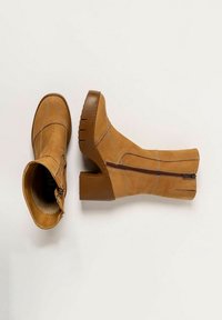 Botas de tobillo de cuero marrón claro con tacón cuadrado, que presentan costuras decorativas y una cremallera lateral. Textura suave y diseño de punta redonda.