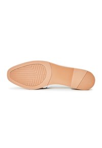 Sole of a shoe with a smooth tan rubber bottom, featuring a zigzag pattern and a slight heel for traction. White upper edge visible.