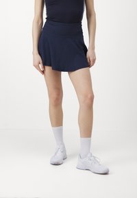 Navy blue tennis skirt with a wide waistband, flared design, and lightweight fabric, paired with white sneakers and ribbed crew socks.