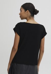Top nero a maniche corte realizzato in tessuto morbido. Presenta una vestibilità comoda con scollatura ampia e una superficie liscia, leggermente texture.