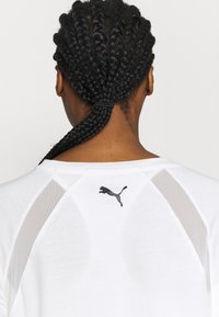 Top deportivo blanco con un logo negro de Puma en la espalda, con detalles de malla transparente en las mangas para mayor transpirabilidad y textura.
