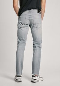 Jeans de mezclilla gris claro con corte ajustado, que cuentan con dos bolsillos traseros y una etiqueta de marca negra en la cinturilla. Combinados con zapatillas blancas.