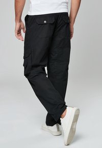 Schwarze Cargohosen mit Taschen, schmaler Passform und robustem Stoff. Kombiniert mit weißen Sneakern, die graue Akzente an der Ferse haben.