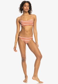 Randig bikiniuppsättning med en bralette-topp och lågt skurna shorts i rostfärg med vita ränder. Tyget är mjukt och elastiskt.