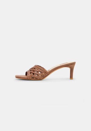Brun åben-tå mule-sandal med flettet læderoverdel og mellemhøj, tilspidset hæl på hvid baggrund.
