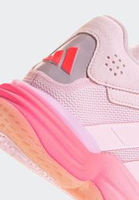 Gros plan sur le talon d'une chaussure de sport rose présentant un tissu en maille, des accents en daim, une semelle rembourrée et un logo de marque rouge sur un panneau gris.