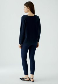 Pull oversized bleu marine avec encolure bateau, associé à des leggings bleu marine ajustés et des chaussures à talons ouverts noires, présenté de vue latérale arrière.