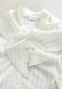 Biała bluzka z cienkimi czarnymi paskami, z luźnym kołnierzem i miękkim, teksturowanym materiałem. Zapięcie na guziki z przodu.