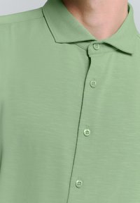 Lichtgroene poloshirt met korte mouwen, een gestructureerde afwerking, een platte kraag en vier bijpassende knopen langs de sluiting.