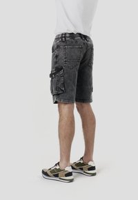 Pantalones cortos cargo grises con una cintura, que presentan múltiples bolsillos, detalles cosidos y una textura desgastada. Combinados con zapatillas negras y beige.