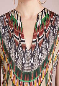 Mnohobarevné šaty s hlubokým V výstřihem, geometrickými vzory v zelené, červené, černé a bílé barvě a texturovanou, lehkou tkaninou.