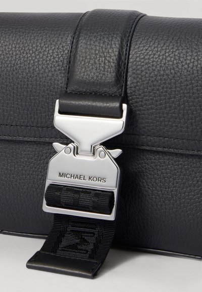 Sac en cuir grainé noir doté d'une fermeture métallique argentée gravée "MICHAEL KORS" et d'une sangle texturée pour une fixation sécurisée.
