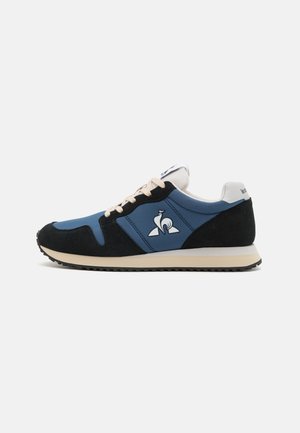 Zapatillas deportivas con un upper de textil azul y acentos de ante negro, cordones en un tono beige claro y un contrafuerte blanco con detalles del logotipo.