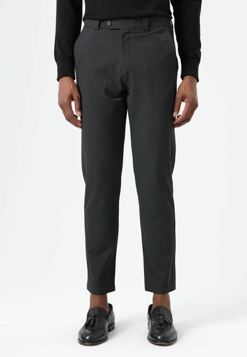 Graue, maßgeschneiderte Hosen mit schlanker Passform, vorderer Knopfverschluss und seitlichen Taschen, kombiniert mit schwarzen Loafers. Glatte Textur und klassisches Design.