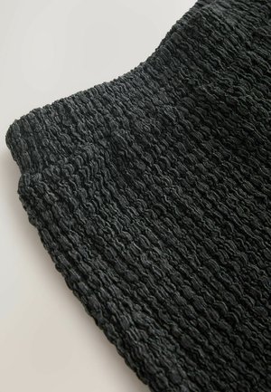 Schwarz strukturierter Stoff mit einem zerknitterten Design und einer weichen Oberfläche, der ein Wellenmuster zeigt. Die Kanten sind glatt und leicht gebogen.