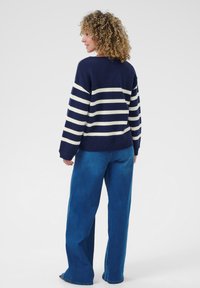 Maglione a righe navy con linee crema, texture a maglia, scollo a girocollo, spalle basse, abbinato a jeans blu a gamba larga.