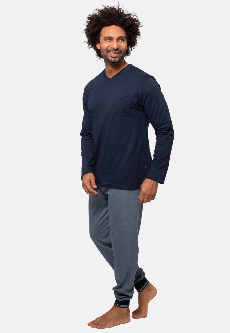 Navyblaues Langarm-V-Ausschnitt-Shirt mit einer Tasche auf der linken Brust, kombiniert mit grauen Jogginghosen mit Knöchelbündchen und kontrastierenden Streifen.