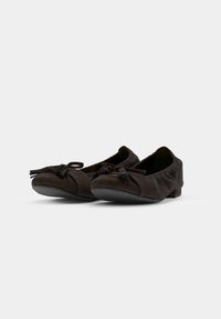 Ballerines en cuir marron foncé avec un design plissé, semelle plate en caoutchouc, et un nœud décoratif avec des franges sur le bout.