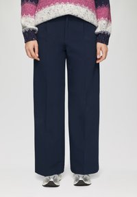 Marineblauwe wijde broek gemaakt van stof met een gladde textuur, met voorplooien en een rechte snit. Gecombineerd met zilveren sportieve schoenen.