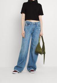 Avklippt svart skjorta, löst sittande ljusblå jeans med slitna detaljer, och en grön tygväska. Skorna är vinröda med vita sulor.