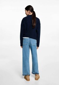 Marinblå tröja med avslappnad passform, i kombination med ljusblå vida jeans och bruna ankelstövlar. Slät textur och standard femfickorsdesign.