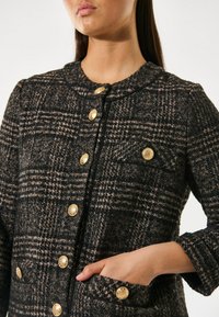 Texturierte schwarze und braune karierte Jacke mit runden Kragen, goldenen Knöpfen und Taschen. Sie hat ein tailliertes Design und Dreiviertelärmel.