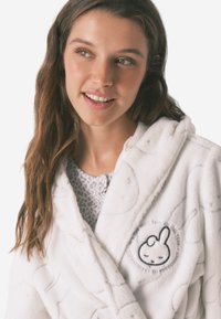 Hvid plysset morgenkåbe med en blød tekstur, hætte og broderet kaninmotiv. Mønsteret inkluderer subtile prikkede accenter overalt.