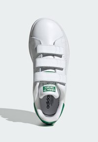 Baltā ādas sporta apavu ar trim Velcro siksnām, noapaļota purngala, zaļiem akcentiem uz zoles un logotipa, teksturētu odere un minimāla šuvju izmantošana.