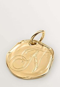 Colgante de oro, forma circular con un borde ligeramente irregular, que presenta la letra "N" grabada en cursiva. Superficie lisa y brillante con un lazo para su sujeción.