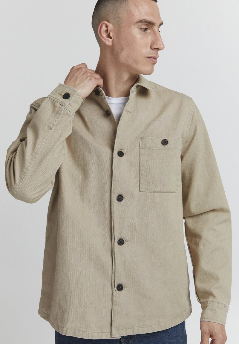 Beige overhemd met lange mouwen, gemaakt van katoen, met een knoopsluiting aan de voorkant, borstzak en zwarte knopen die het ontwerp accentueren.