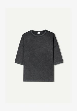 Maglietta a maniche corte oversize di colore grigio scuro, realizzata in cotone. Presenta un collo rotondo e cuciture visibili lungo i bordi.