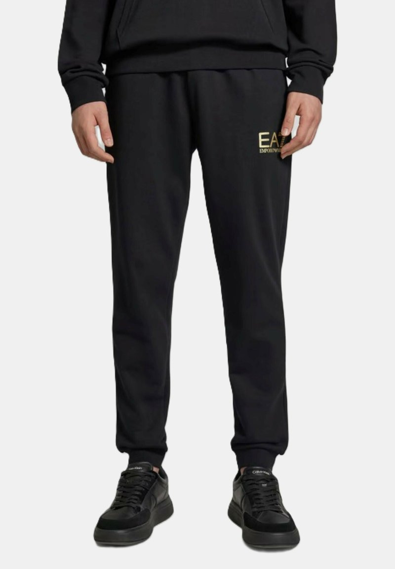 Pantaloni tuta neri realizzati in tessuto morbido, con un design affusolato, vita elastica e logo dorato "EA" sulla coscia sinistra.