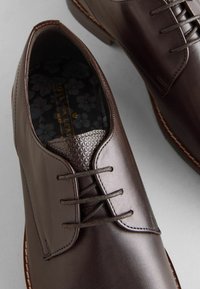 Braune Lederschuhe mit glatter Oberfläche, Schnürdesign, strukturierten Akzenten am Kragen und mit Blumenmuster gefüttertem Innenraum.