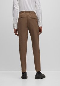 Bruna byxor med elastisk midja, slim fit och två bakfickor. Bärs med en vit skjorta och svarta skor.