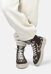 Hochformat-Sneaker mit einem braunen und Leopardenmuster, Materialien aus Wildleder und glattem Leder, einer strukturierten, cremfarbenen Gummisohle und hellen Schnürsenkeln.