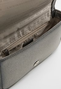 Borsa metallic gray con superficie testurizzata, dotata di tasca con zip e tessuto interno che riporta il nome del marchio in un motivo ripetuto.