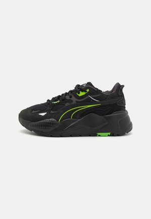 Czarny sportowy sneaker z neonowo zielonymi akcentami, grubą podeszwą oraz materiałami z siateczki i zamszu, widoczny z boku na jednolitym tle.