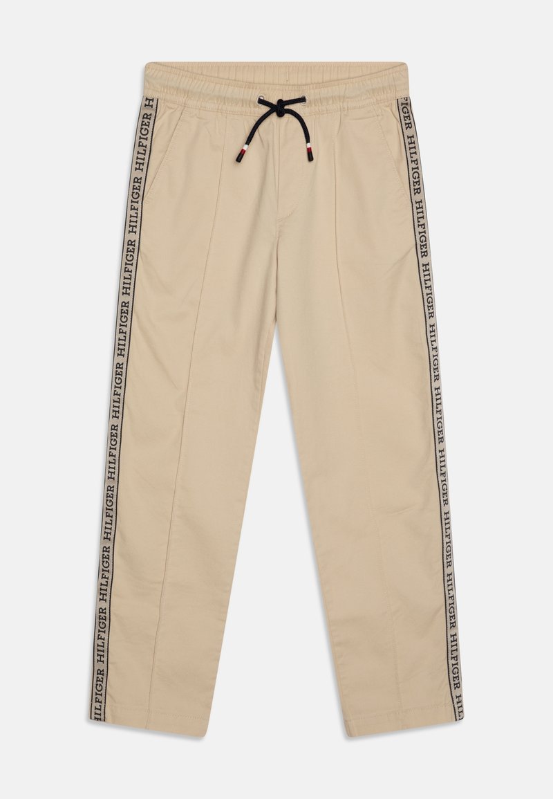 Beige joggingbroek met een elastische tailleband en een zwart trekkoord. De zijnaden hebben een zwart-wit "HILFIGER" logo bandaccent.