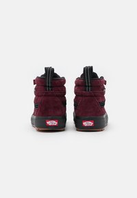 burgunderfargede semskede høye sneakers med svarte detaljer, teksturert materiale, polstret krage og gummisåle med en rød merkeetikett på hælen.