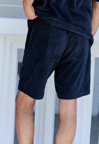 Pantalones cortos de rizo azul marino con un patrón de diamante texturizado, de longitud media, que cuentan con dobladillo cosido y bolsillos laterales.