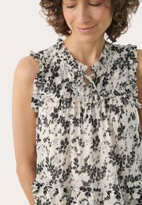 Bluză florală cu modele în alb și negru, guler ondulat, detaliu cu deschidere și tiv în straturi. Țesătură ușoară, moale, cu o croială lejeră.