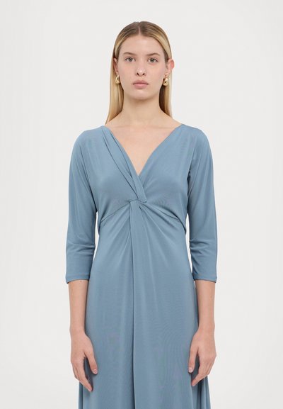 Blauwe wikkeljurk van zachte, elastische stof met een V-hals, 3/4 mouwen en een gedraaide detail bij de taille. Glad textuur, minimalistisch ontwerp.