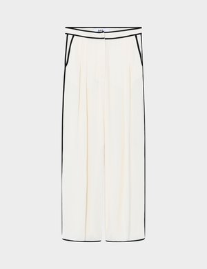 Pantalon large couleur crème avec un liseré noir le long de la taille, des poches, des côtés et des ourlets, doté de plis à l'avant et d'une fermeture frontale dissimulée par boutons.