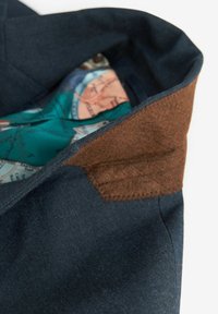 Granatowy materiał o teksturowanym wykończeniu z brązowymi akcentami z zamszu. Wewnątrz znajduje się kolorowy wzór mapy na zielonym tle.