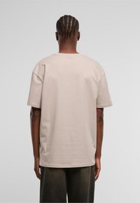 Beige oversized bomulls T-skjorte med korte ermer og rund hals, med et enkelt design og en avslappet passform, sett bakfra.